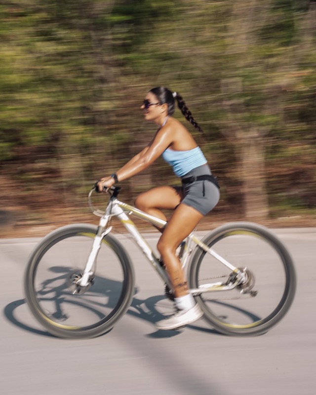 A cyclist in sunglasses rides past a blurred green roadside.