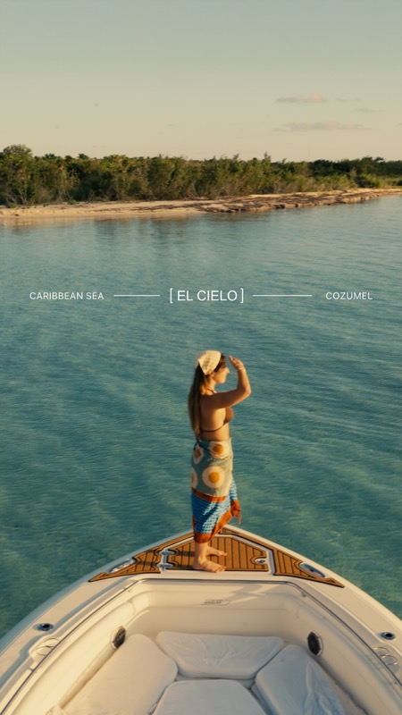 A woman stands on the bow of a boat above clear turquoise water near Cozumel.